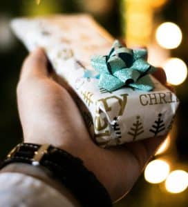 Pic of a man handing over a well-wrapped unique Christmas gift withh a pretty bow